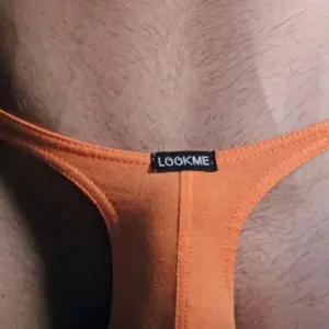 String masculin orange ajustable, vue de près, en coton élasthanne, étiquette noire visible, design sexy et minimaliste.