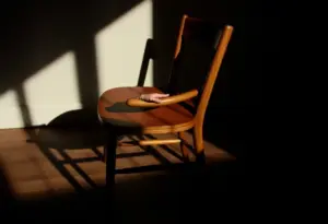 Une chaise en bois dans une pièce sombre, mains posées sur le bras
